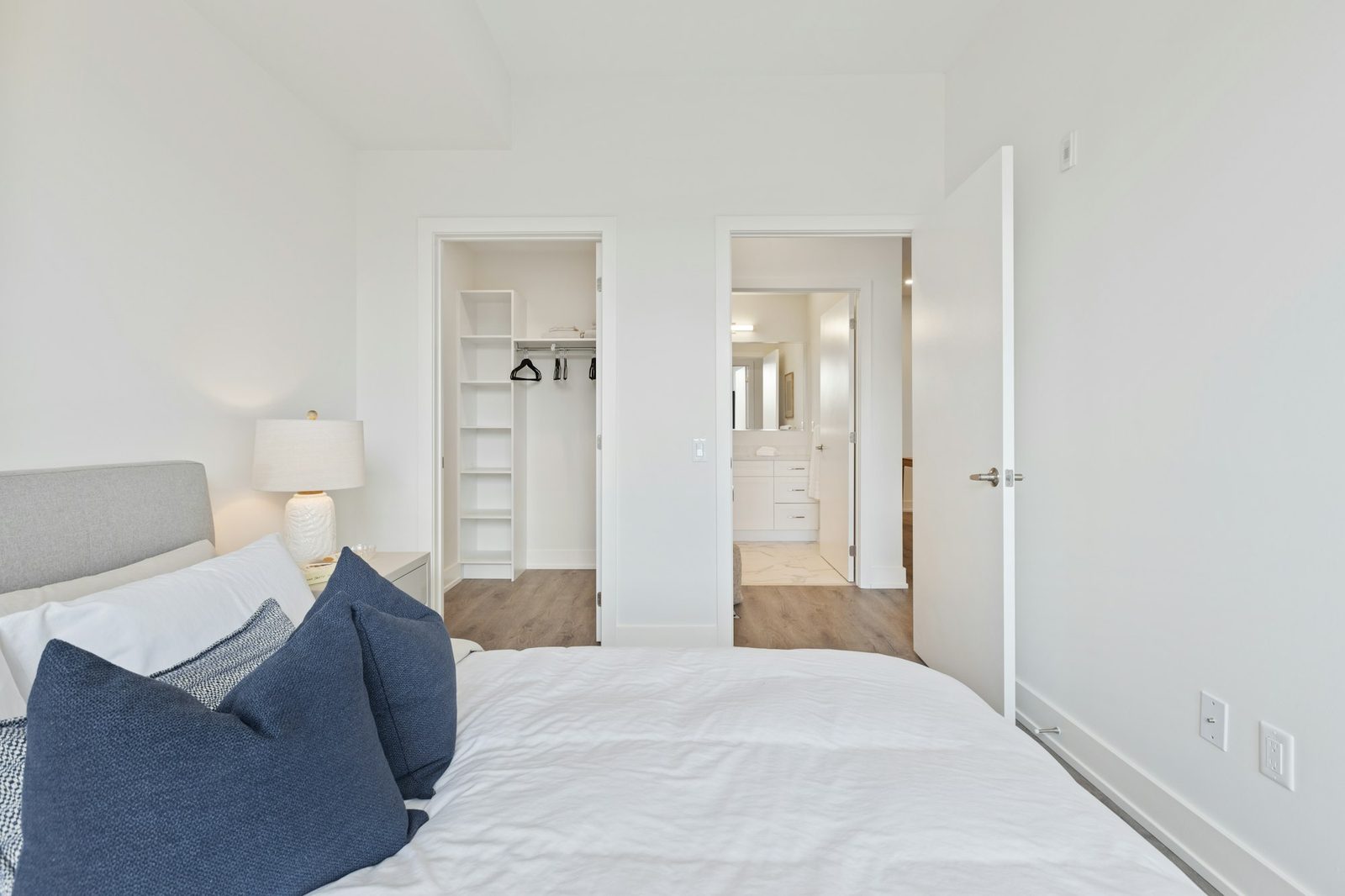 Bedroom with a large bed, white linen and blue pillows, and a closet and bathroom through the doorway