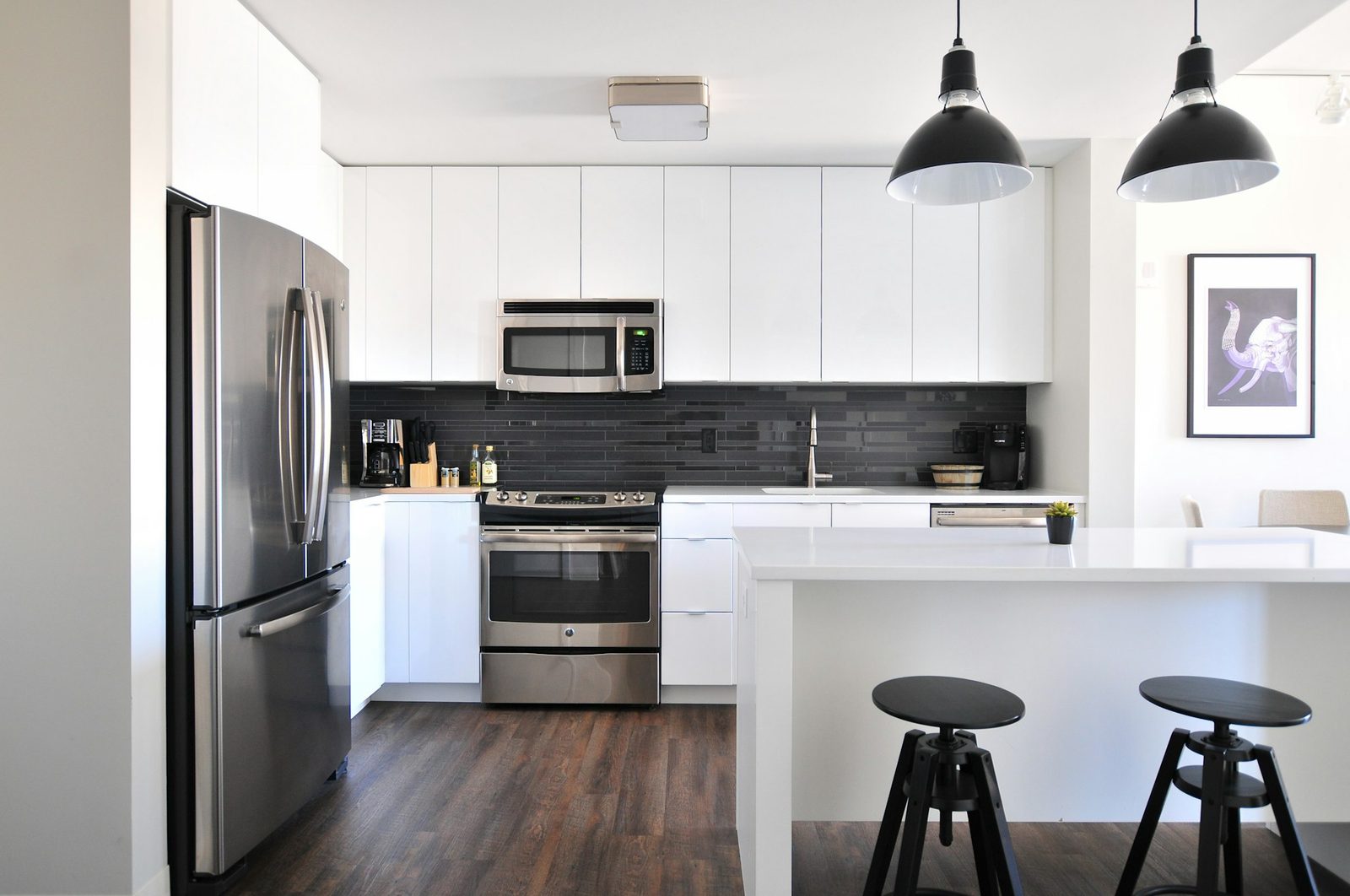 Bright kitchen with white cabinets, stainless steel appliances, an island and two black stools