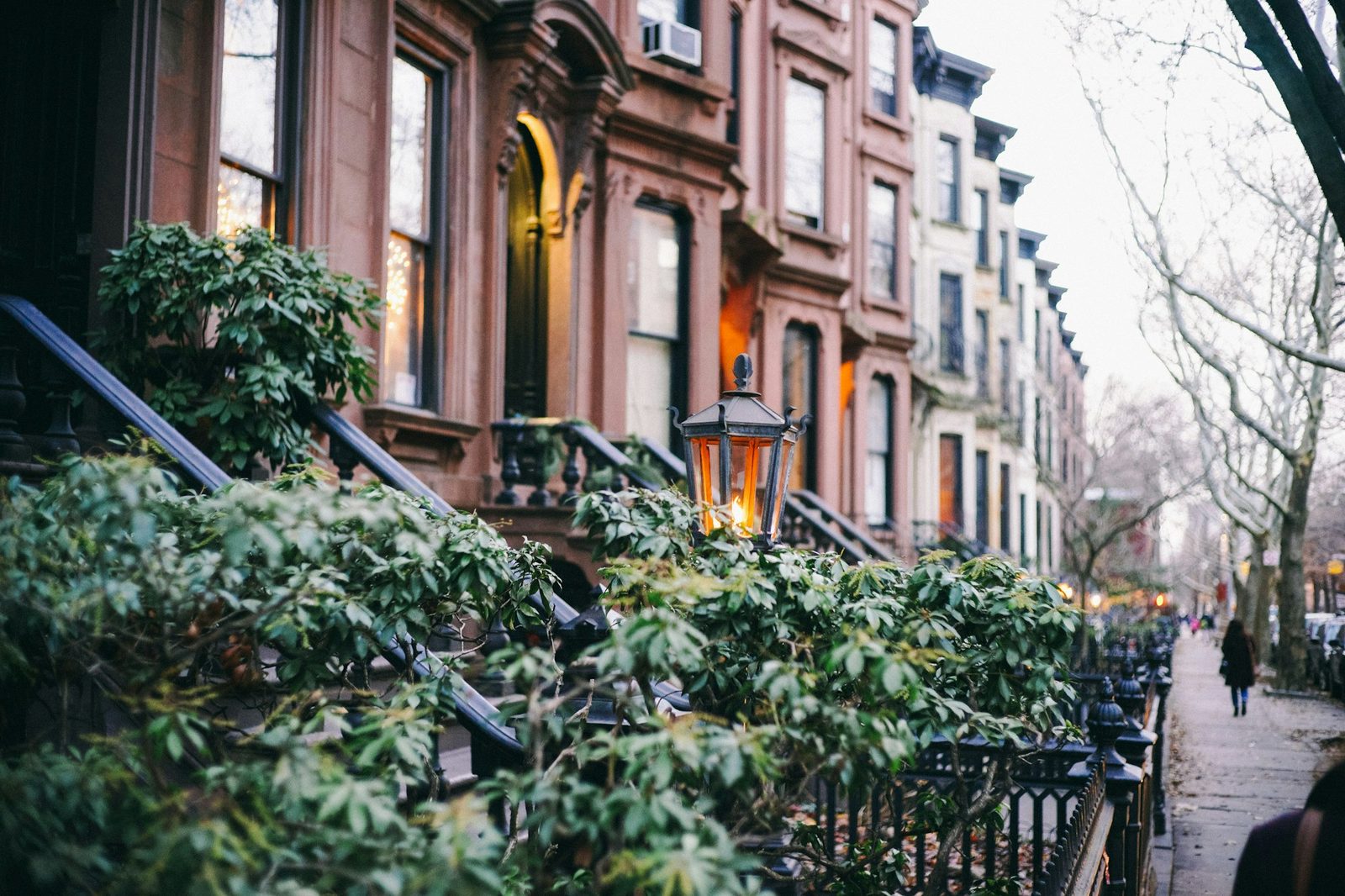 Brownstone-style townhouses with stoops, lanterns and leafy front gardens on a tree-lined street