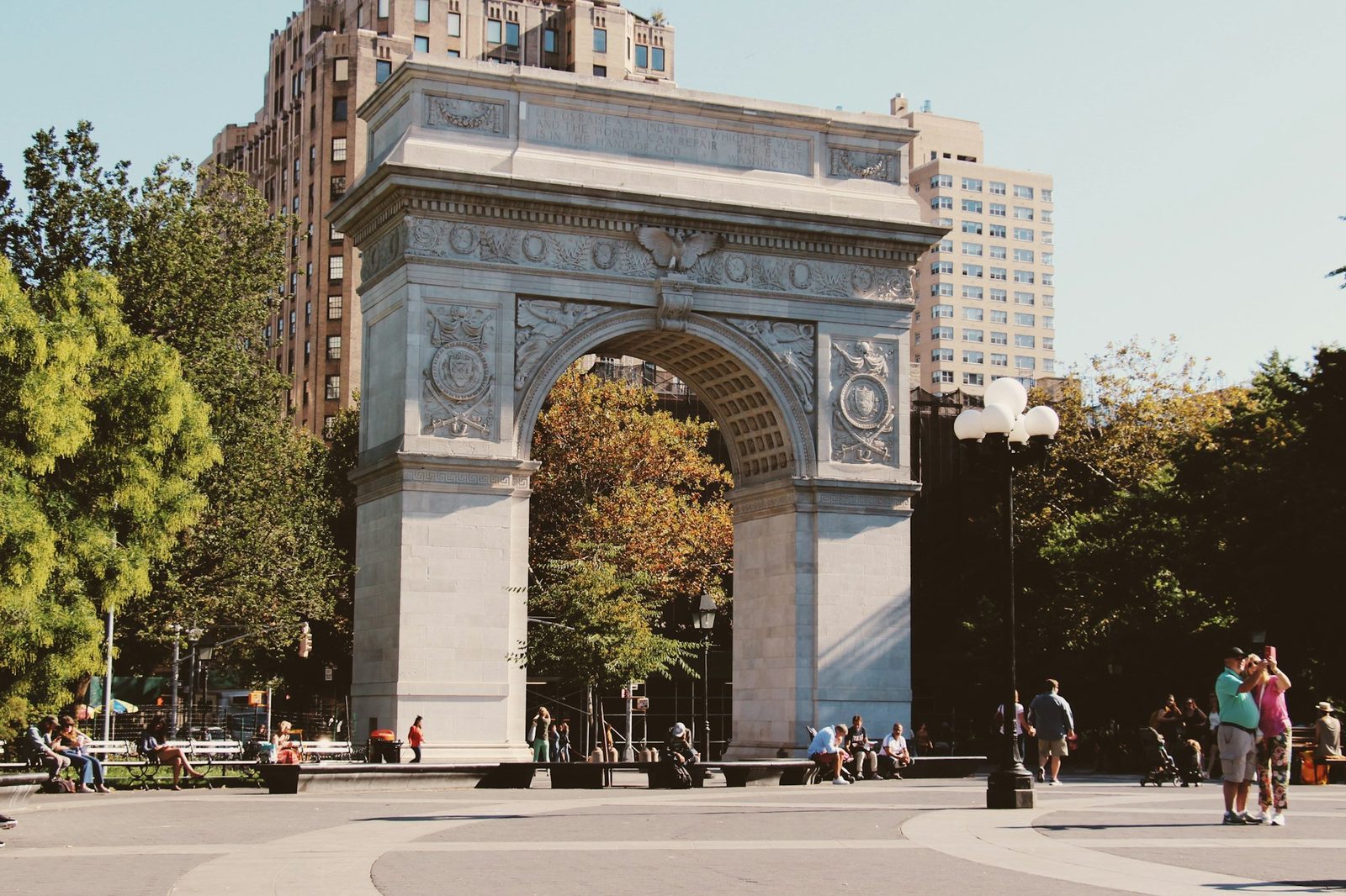 The marble Washington Square Arch with green trees and people in the park