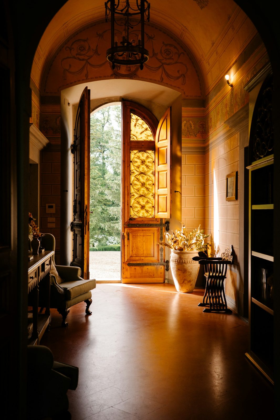 An arched entrance with an open timber door, a lantern overhead and trees visible beyond