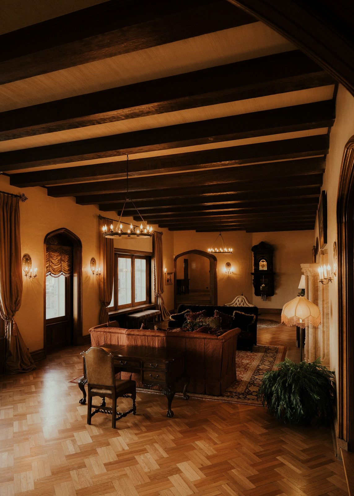 The sitting room, with a dark beamed ceiling, a herringbone parquet floor, armchairs and warm lamplight