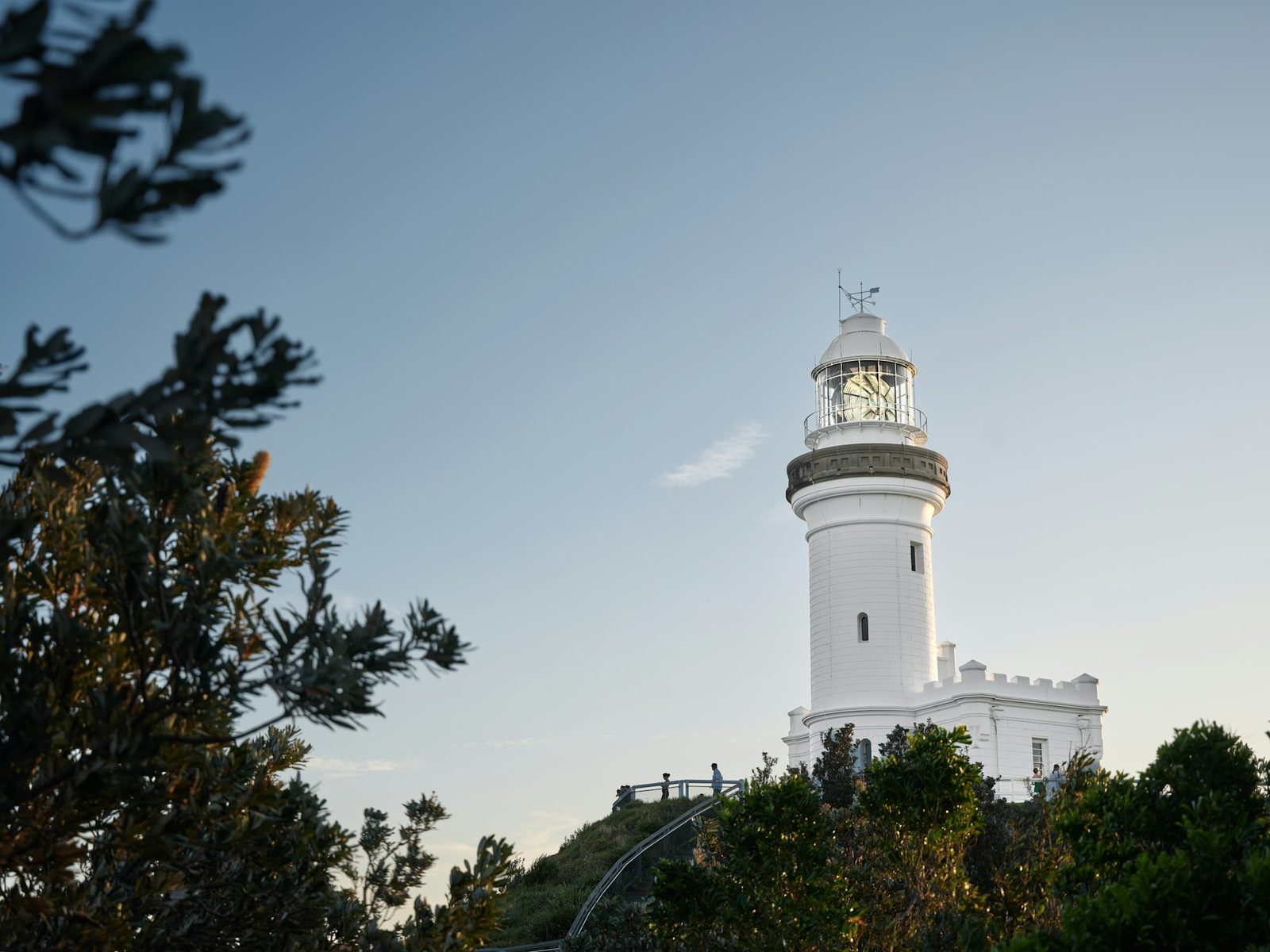 A white lighthouse with a black-banded lantern and a low castellated base, on a green headland.
