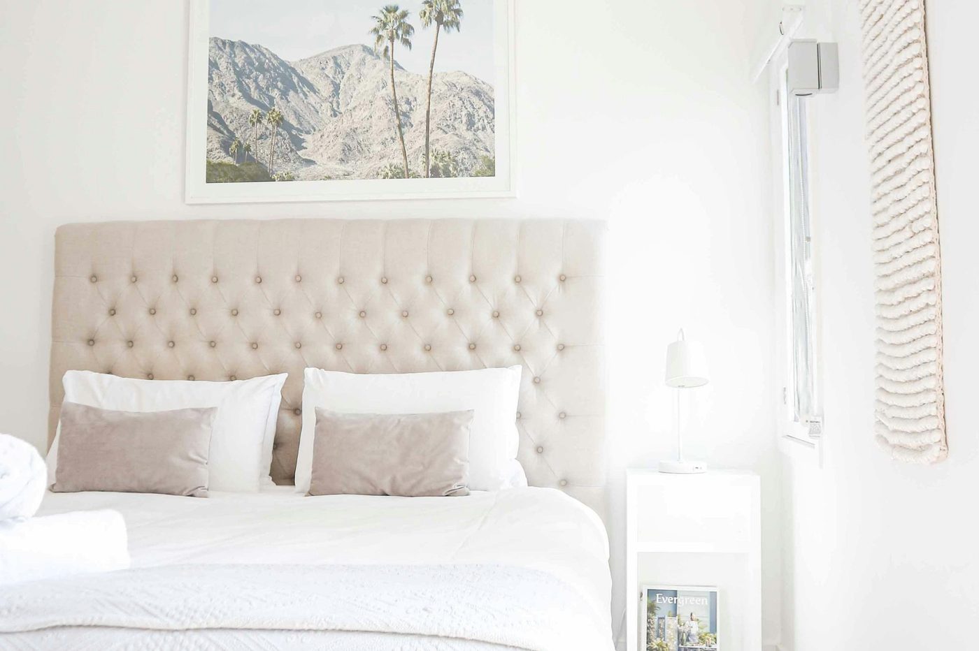 A white bedroom with a queen bed and a tufted bedhead, a ceiling fan and timber floors
