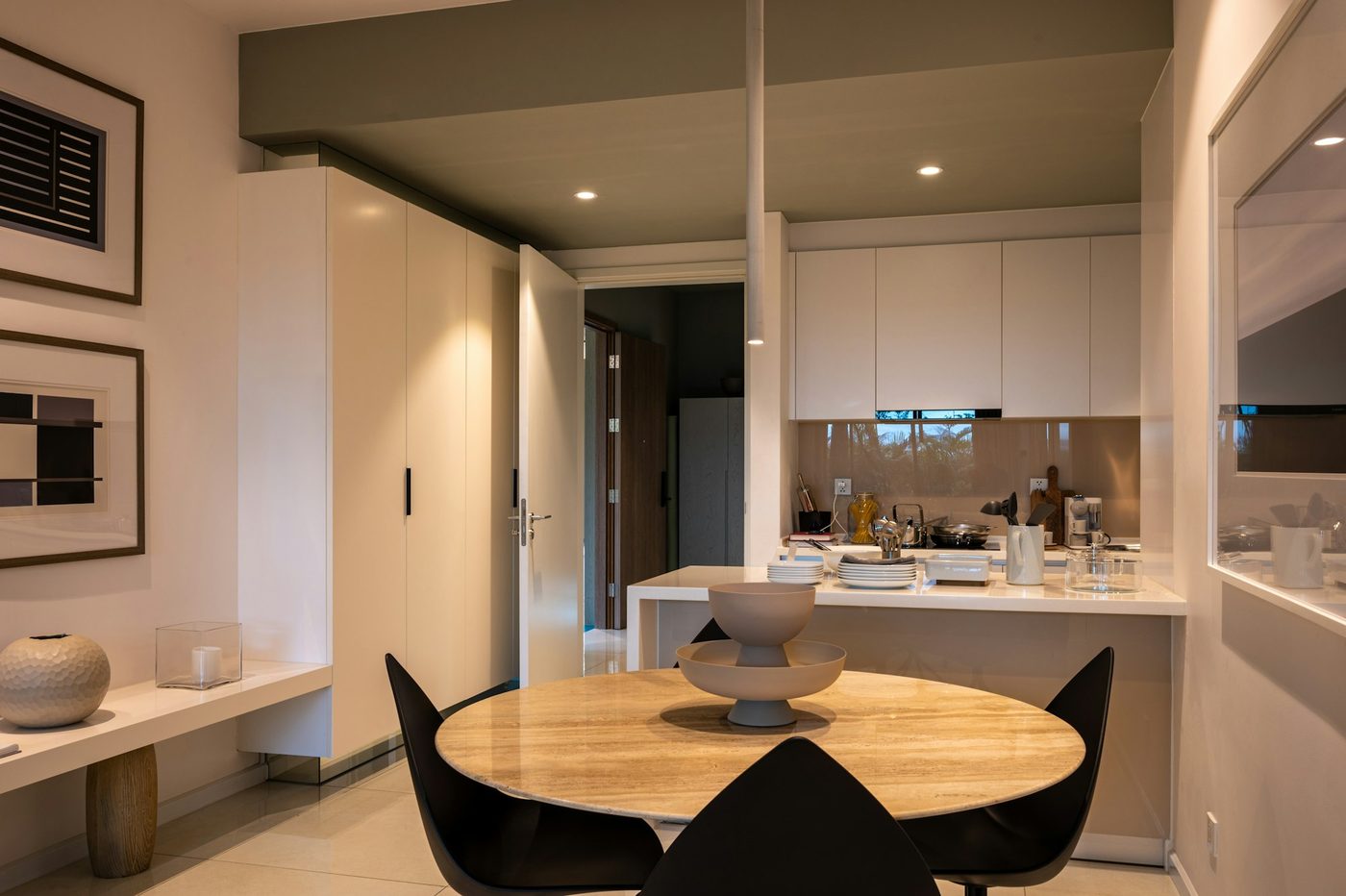 A kitchen with white cabinets and a round table with black chairs, lit by downlights